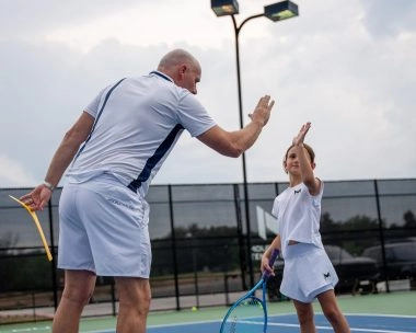 Tennis coach and young player sharing a high-five on an outdoor court.
