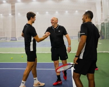 Tennis coach instructing two players on an outdoor court at Mouratoglou Academy Malaysia.