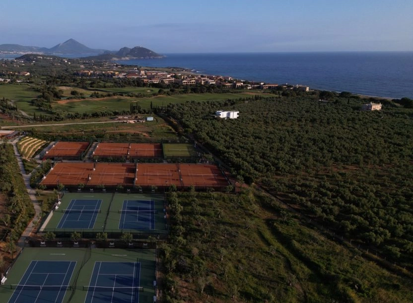 Aerial view of tennis courts near the coastline surrounded by nature.