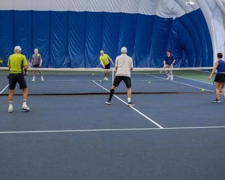 Players competing in an indoor doubles tennis match inside a covered dome court.