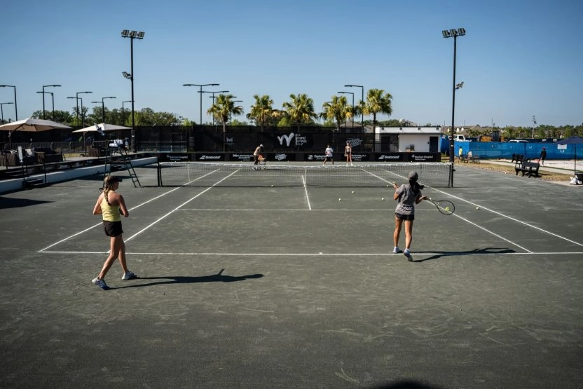 Wide view of players training on an outdoor tennis court under a clear sky
