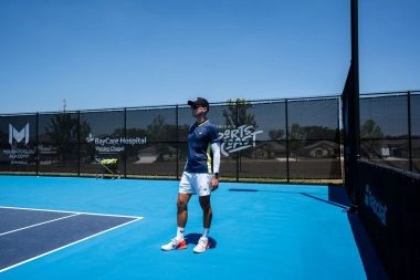 Tennis coach instructing players on a sunlit outdoor court at Mouratoglou Academy Zephyrhills.