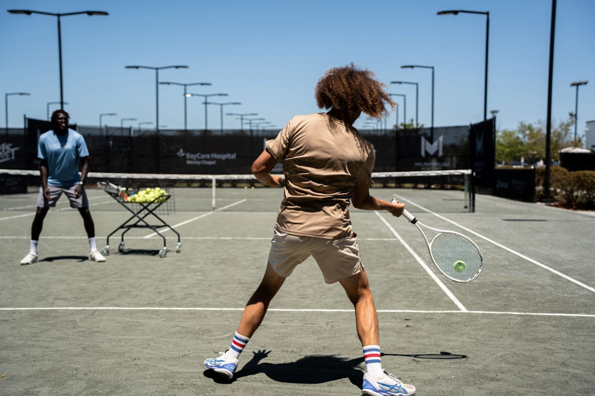 Tennis player hitting a forehand during an outdoor training session with a coach on court