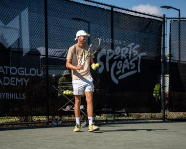 Tennis coach holding balls and racket on court at Mouratoglou Academy Zephyrhills Florida.
