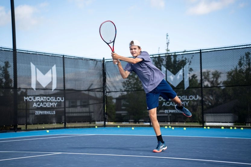 Tennis player hitting a forehand during an outdoor training session with a coach on court