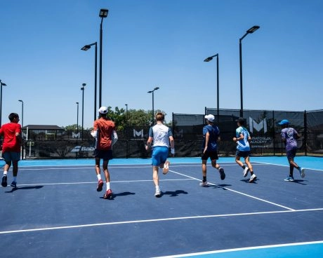 Group of young tennis players doing warm-up runs on a blue court