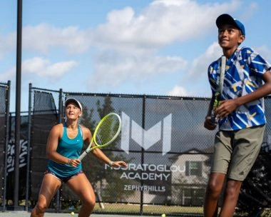 Teen and adult tennis players training together on an outdoor court