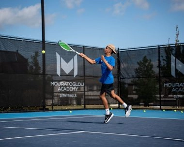 Young tennis player hitting a forehand on an outdoor court at Mouratoglou Academy