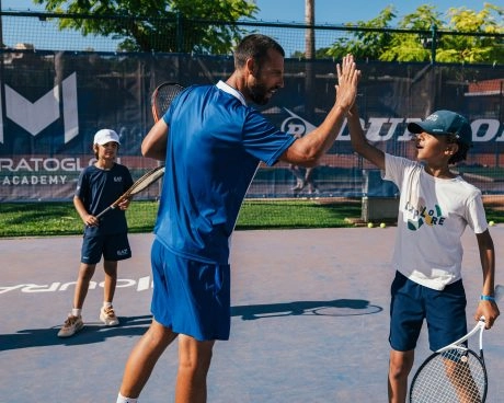 Entraîneur de tennis donnant un high-five à un jeune joueur pendant un entraînement.
