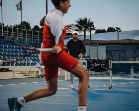 Young tennis player hitting a forehand during a coached training session on an outdoor court
