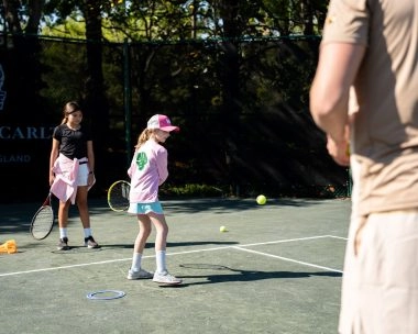 Child waiting to return a ball under the supervision of a coach at Mouratoglou Tennis Center Amelia Island