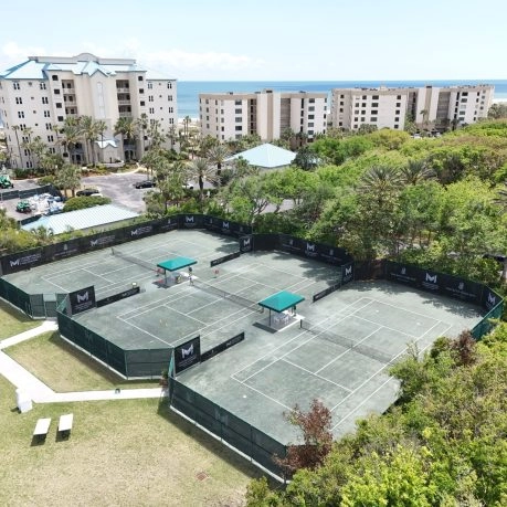 Three Mouratoglou Tennis Center courts surrounded by palm trees and sunshine
