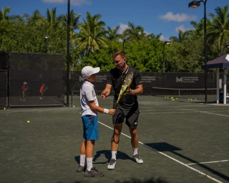 Tennis coach giving guidance to a young player during training on an outdoor court