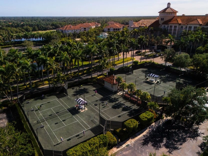 Aerial view of outdoor clay tennis courts surrounded by palm trees at a resort