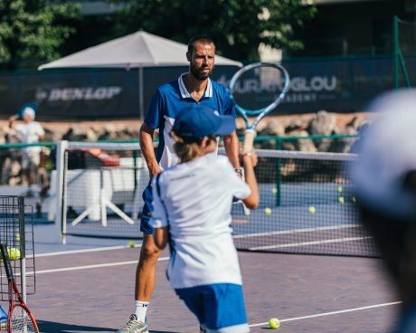 Tennis coach guiding a young player during a training session on court.