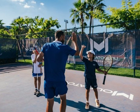 Coach de tennis félicitant de jeunes joueurs avec un high five sur un court extérieur