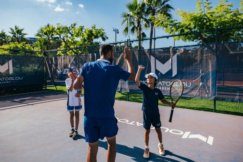 Coach de tennis félicitant de jeunes joueurs avec un high five sur un court extérieur