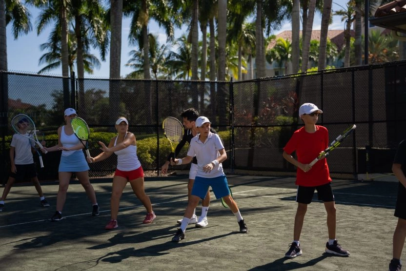 Group tennis drill with players practicing on an outdoor palm-lined court