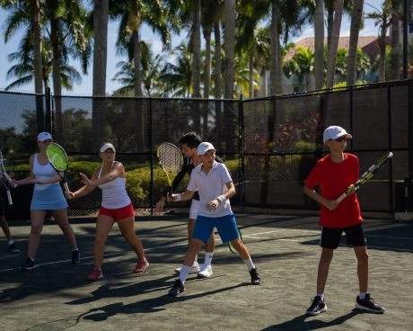 Group tennis drill with players practicing on an outdoor palm-lined court