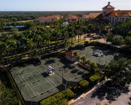 Aerial view of outdoor clay tennis courts surrounded by palm trees at a resort