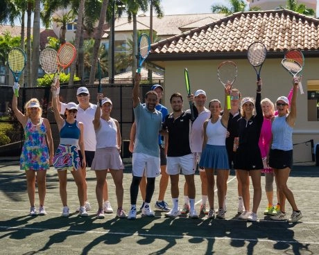Group of adult tennis players posing with raised rackets on an outdoor court at a sunny resort