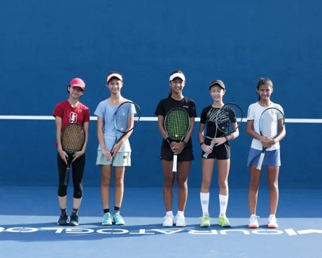 Group of junior tennis players standing with their rackets on a blue court