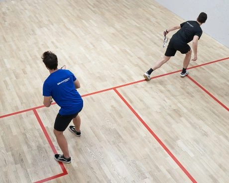Two squash players practicing on an indoor wooden court.