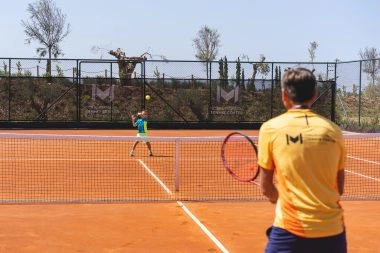 A young player being trained by a coach on clay court