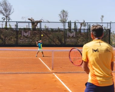 A young player being trained by a coach on clay court