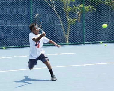Young tennis player running to hit a forehand on a blue court during training