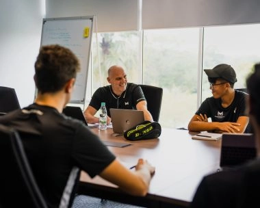 Coach leading a wellbeing and personal care meeting with students around a table