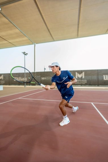 Tennis coach demonstrating a racket swing on the courts of Mouratoglou Tennis Center Hudayriyat Island in Abu Dhabi, teaching proper technique to players.
