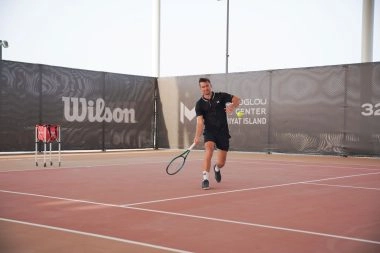 Tennis player receiving a ball on the courts of Mouratoglou Tennis Center Hudayriyat Island in Abu Dhabi, focusing on timing and control.