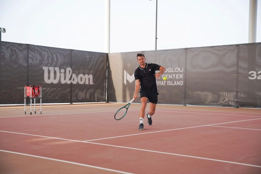 Tennis player receiving a ball on the courts of Mouratoglou Tennis Center Hudayriyat Island in Abu Dhabi, focusing on timing and control.
