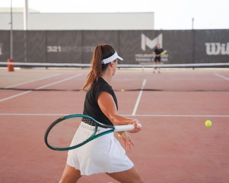 Female player training with her coach on the tennis courts of Mouratoglou Tennis Center Hudayriyat Island in Abu Dhabi, practicing technique and movement.