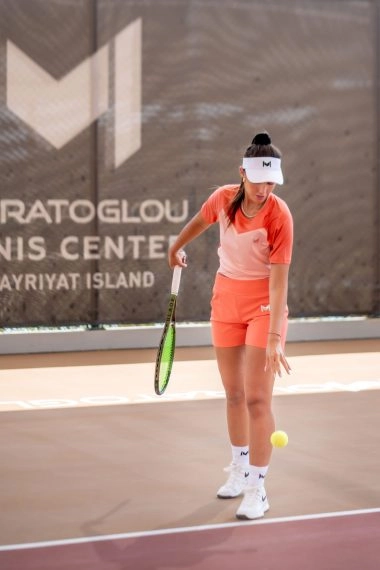Female tennis player preparing to serve on the courts of Mouratoglou Tennis Center Hudayriyat Island in Abu Dhabi, focused and ready for action.