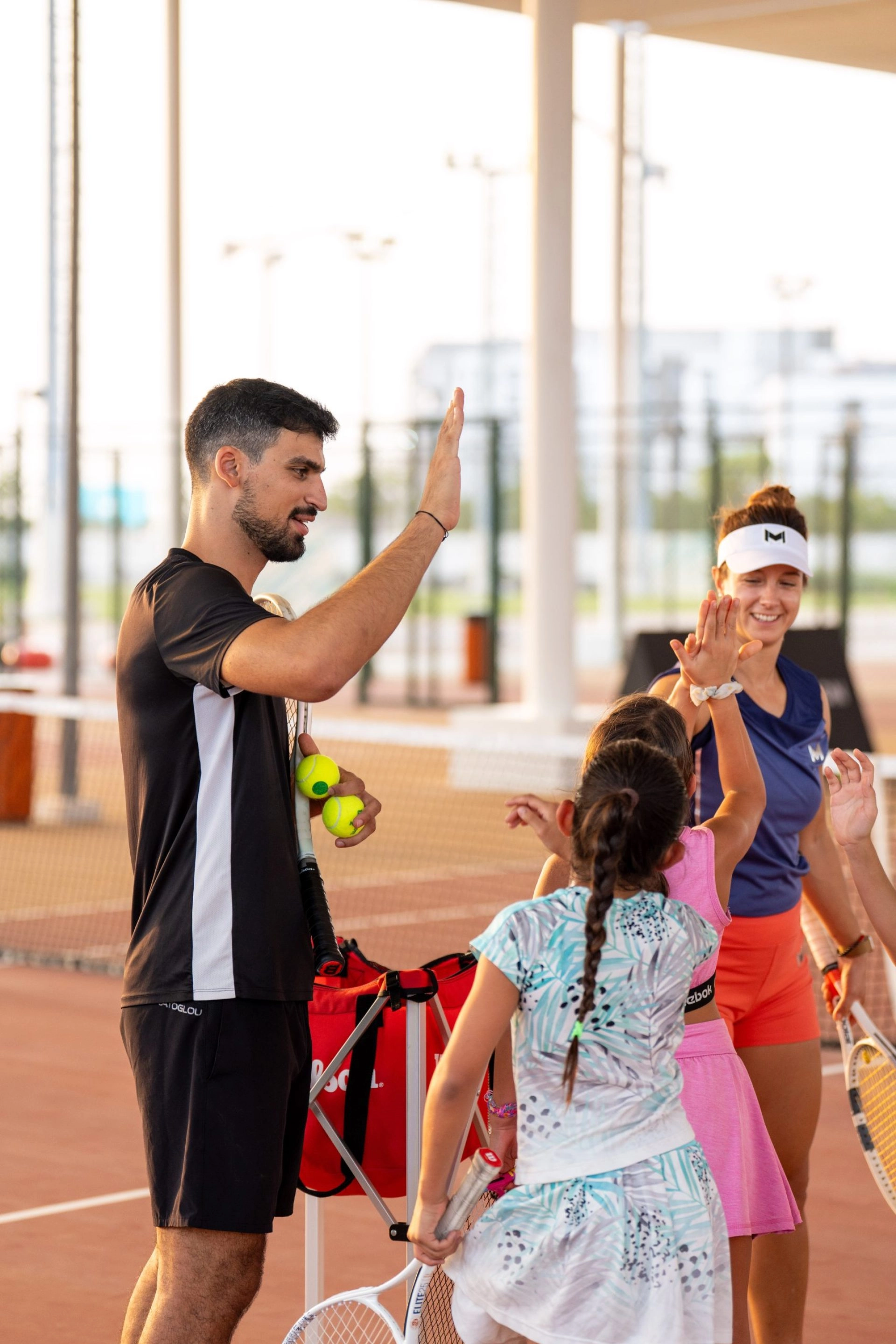 Tennis coach giving a high five to young players at Mouratoglou Tennis Center Hudayriyat Island in Abu Dhabi, celebrating teamwork and progress.