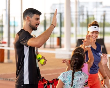 Tennis coach giving a high five to young players at Mouratoglou Tennis Center Hudayriyat Island in Abu Dhabi, celebrating teamwork and progress.