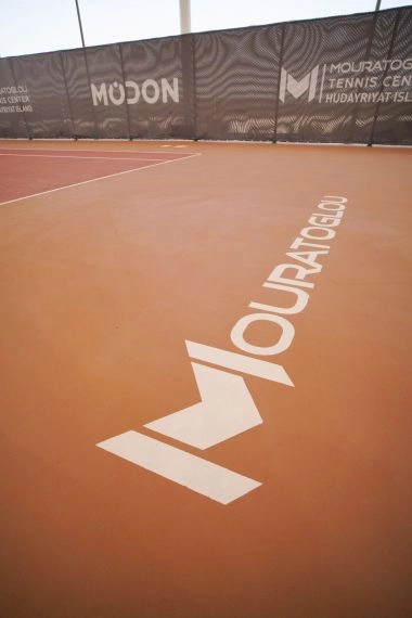 Mouratoglou logo stencil on the tennis court surface at Mouratoglou Tennis Center Hudayriyat Island in Abu Dhabi.