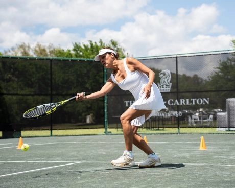 A woman executing a tennis stroke on an outdoor court at Mouratoglou Tennis Center, Ritz-Carlton Amelia Island.