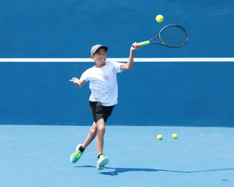Young tennis player jumping to hit a forehand on a blue court