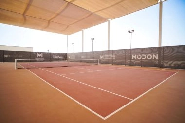 Tennis court at Mouratoglou Tennis Center Hudayriyat Island in Abu Dhabi, featuring high-quality hard surfaces surrounded by palm trees and ocean views.