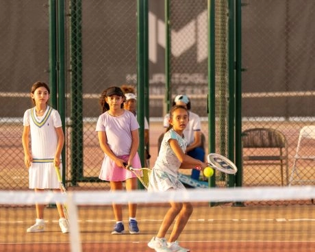 Three young tennis players receiving a ball from their coach on the courts of Mouratoglou Tennis Center Hudayriyat Island in Abu Dhabi during a junior training session.
