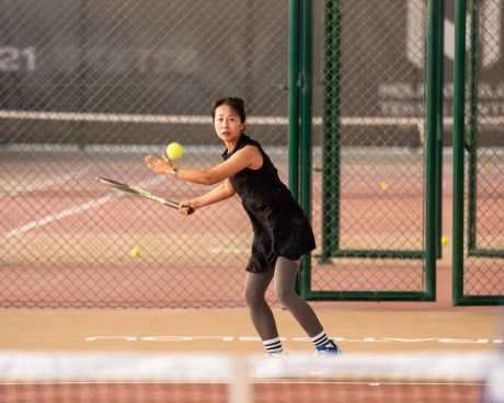 Adult player practicing on the tennis courts of Mouratoglou Tennis Center Hudayriyat Island in Abu Dhabi, surrounded by the sea breeze and palm trees.