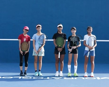 Group of junior tennis players standing with their rackets on a blue court