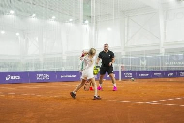 Young tennis player practicing a forehand on an indoor clay court with a coach