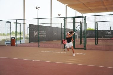 Female tennis player returning a shot on the hard courts of Mouratoglou Tennis Center Hudayriyat Island in Abu Dhabi.