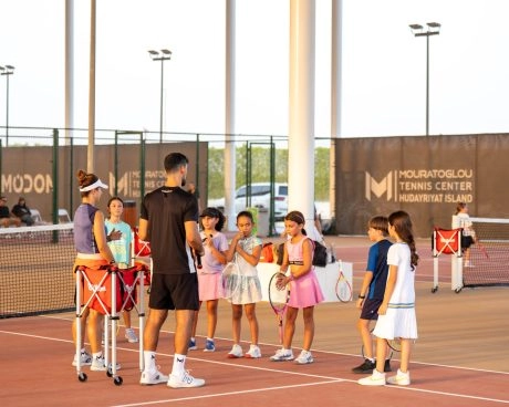 Tennis coach giving instructions to a group of children during a training session on Hudayriyat Island