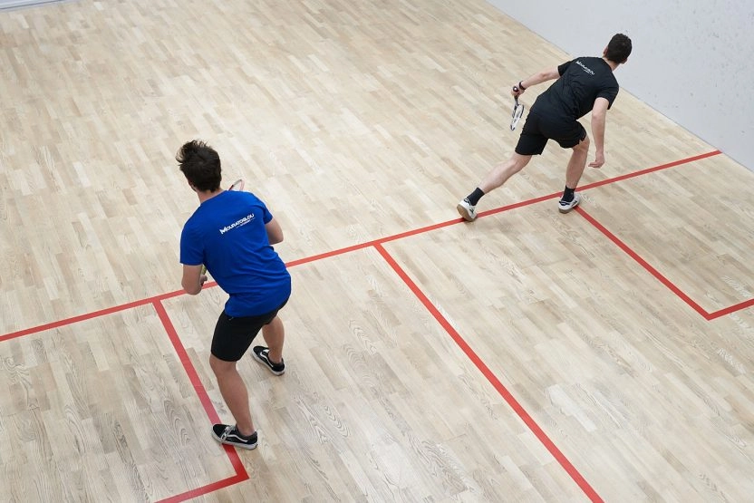 Two squash players practicing on an indoor wooden court