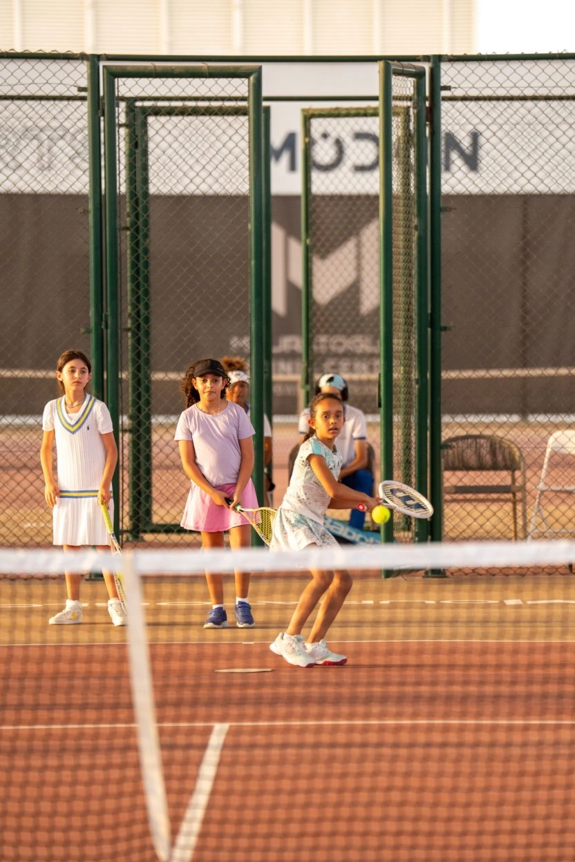 Young girl hitting a forehand during a junior tennis lesson with other children watching